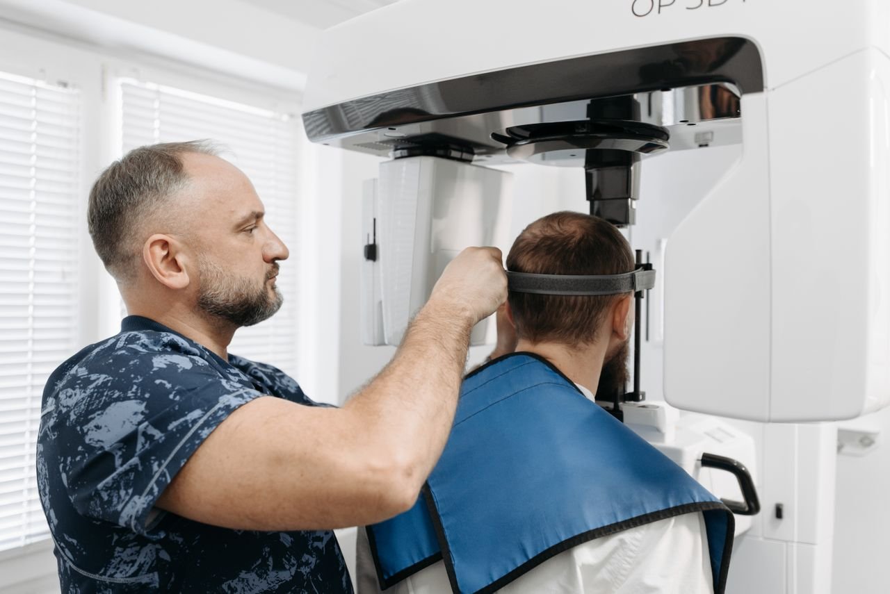 A dentist helps a patient use a dental X-ray machine in a modern office setting.